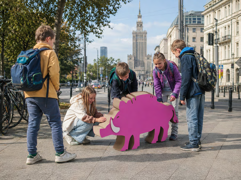 Projekt różowego dzika, a dookoła niego stoją i kucają dzieci.