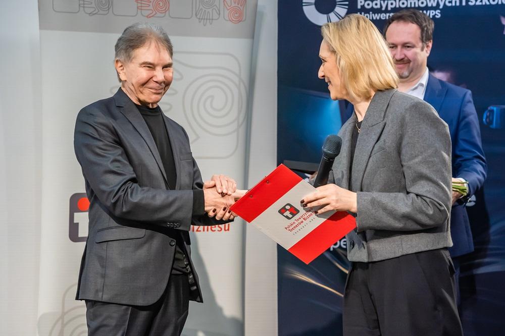 Profesor Cialdini i przedstawicielka Polskiego Towarzystwa Trenerów Biznesu ściskają sobie dłonie przy wręczaniu nagrody