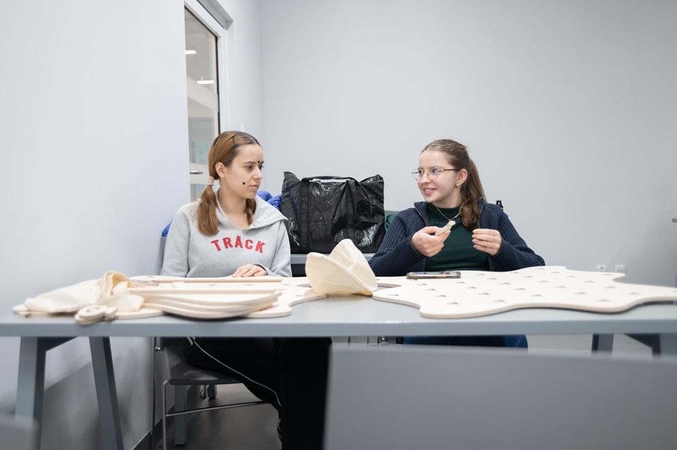 Studentki siedzące przy stoliku, na którym stoją ich projekty wycięte ze sklejki