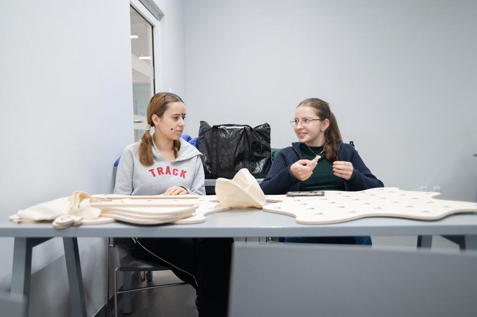 Studentki siedzące przy stoliku, na którym stoją ich projekty wycięte ze sklejki