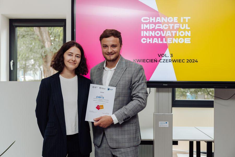 Dwoje członków zespołu Empatia na tle prezentacji z napisem „CHANGE IT – IMPACTFUL INNOVATION CHALLENGE. VOL. 3. KWIECIEŃ–CZERWIEC 2024