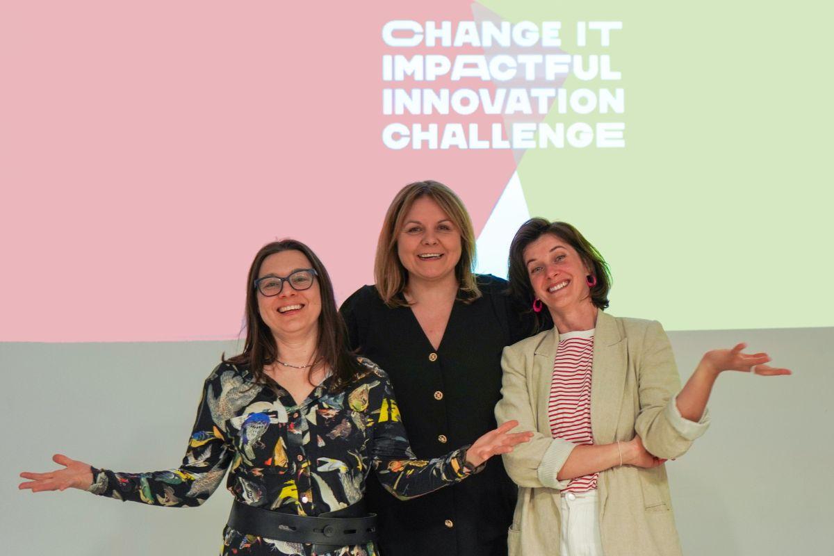Trzy uśmiechnięte kobiety. Nad nimi napis „CHANGE IT. IMPACTFUL INNOVATION CHALLENGE”