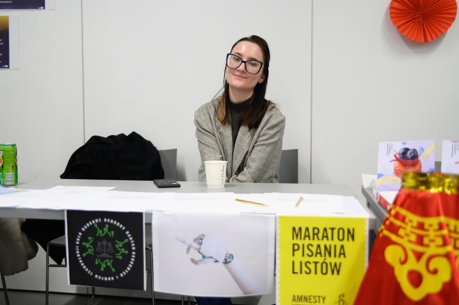 Stoisko z rozłożonymi kartkami i długopisami oraz plakatem z napisem „Maraton Pisania Listów Amnesty International”