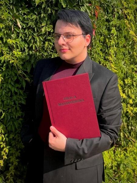Ignacy Maliszewski, absolwent Uniwersytetu SWPS, trzyma w rękach pracę magisterską