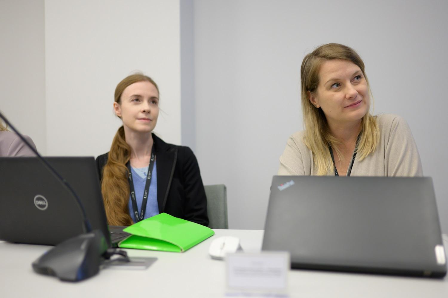 dwie prowadzące konferencje, siedzące przy biurkach przy laptopach