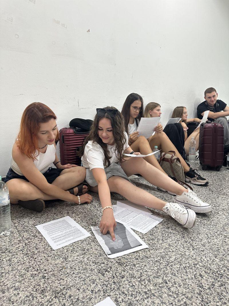 Grupa studentek i studentów USWPS z walizkami studiuje wydrukowane teksty i mapy
