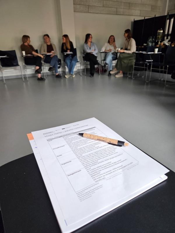 Uczestnicy szkolenia międzykulturowego na Uniwersytecie SWPS w tle; na pierwszym planie notes i długopis