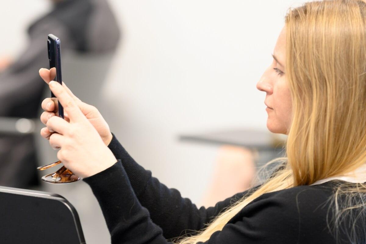 Jasnowłosa kobieta robi zdjęcie telefonem podczas konferencji "Innowacje społeczne. Wyzwania-rozwiązania-praktyki" na Uniwersytecie SWPS