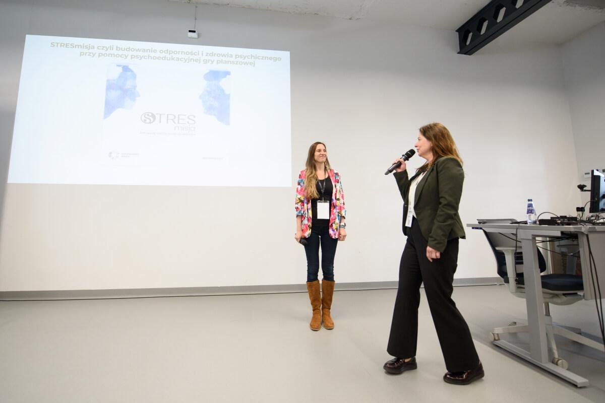 Dr Edyta Bonk i Katarzyna Barcińska z Uniwersytetu SWPS prezentują edukacyjną grę planszową STRESmisja podczas konferencji "Innowacje społeczne. Wyzwania-rozwiązania-praktyki"