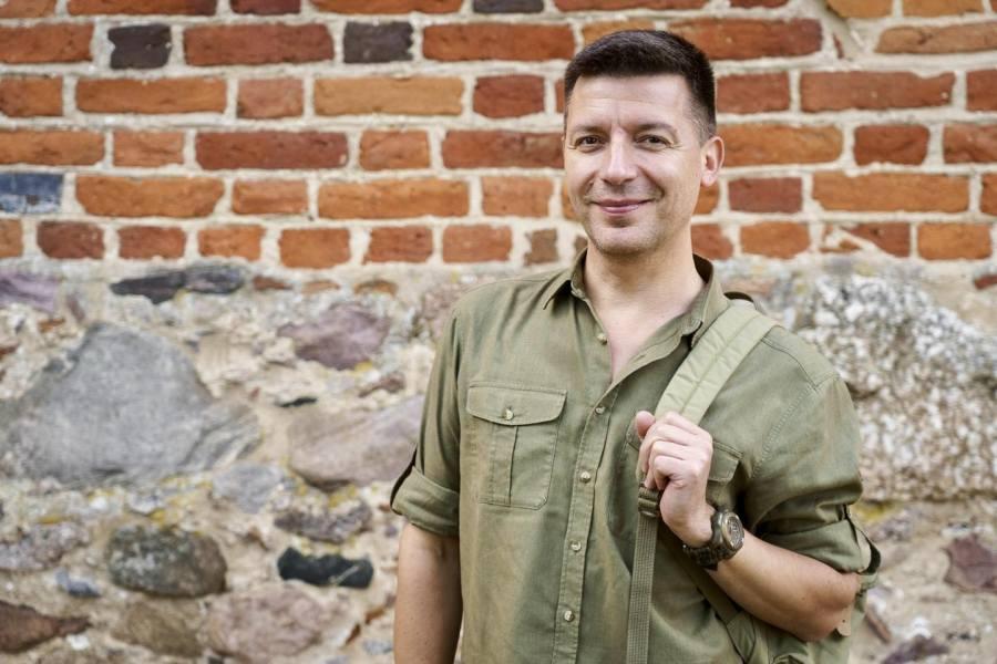 Michał Cessanis z plecakiem stoi na tle ceglanego muru