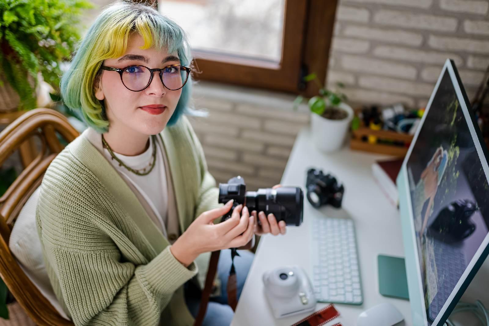 Młoda dziewczyna z aparatem fotograficznym siedząca przed komputerem.