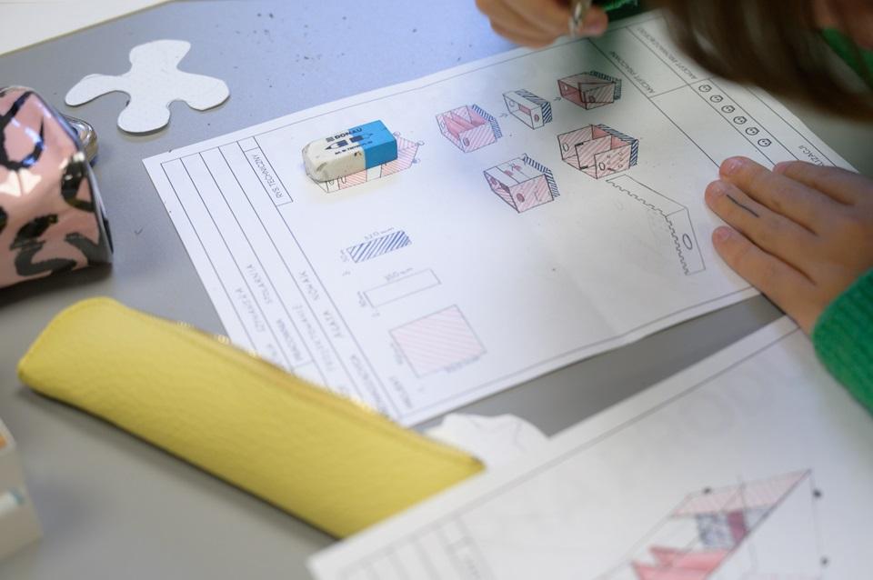 Rozrysowany na kartce papieru plan projektu, obok leżą piórniki i gumka do ścierania