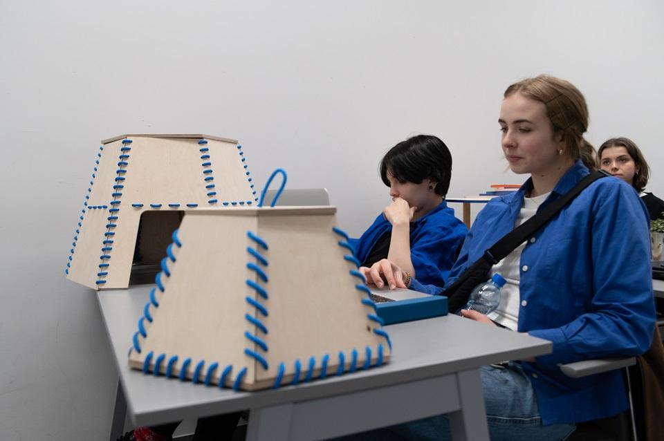Studentki siedzące przy stoliku, na którym stoją ich projekty wycięte ze sklejki